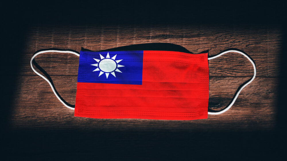 Taiwan National Flag at medical, surgical, protection mask on black wooden background. Coronavirus Covid–19, Prevent infection, illness or flu. State of Emergency, Lockdown