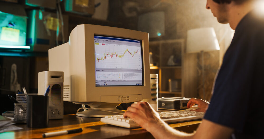 Back View Of Caucasian Male Software Engineer Programming on Old Desktop Computer In Retro Garage. Focused Man Starting Tech Startup Company In Nineties. Coding Innovative Online Service At Home.